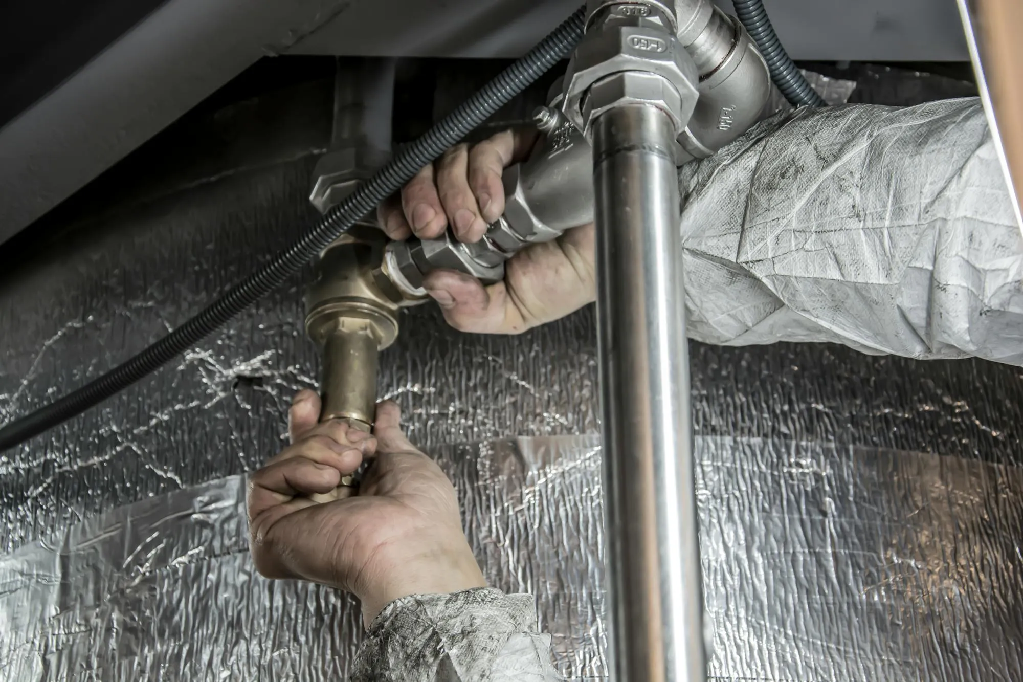 Plumber's hands fitting brass and steel pipe under a kitchen unit